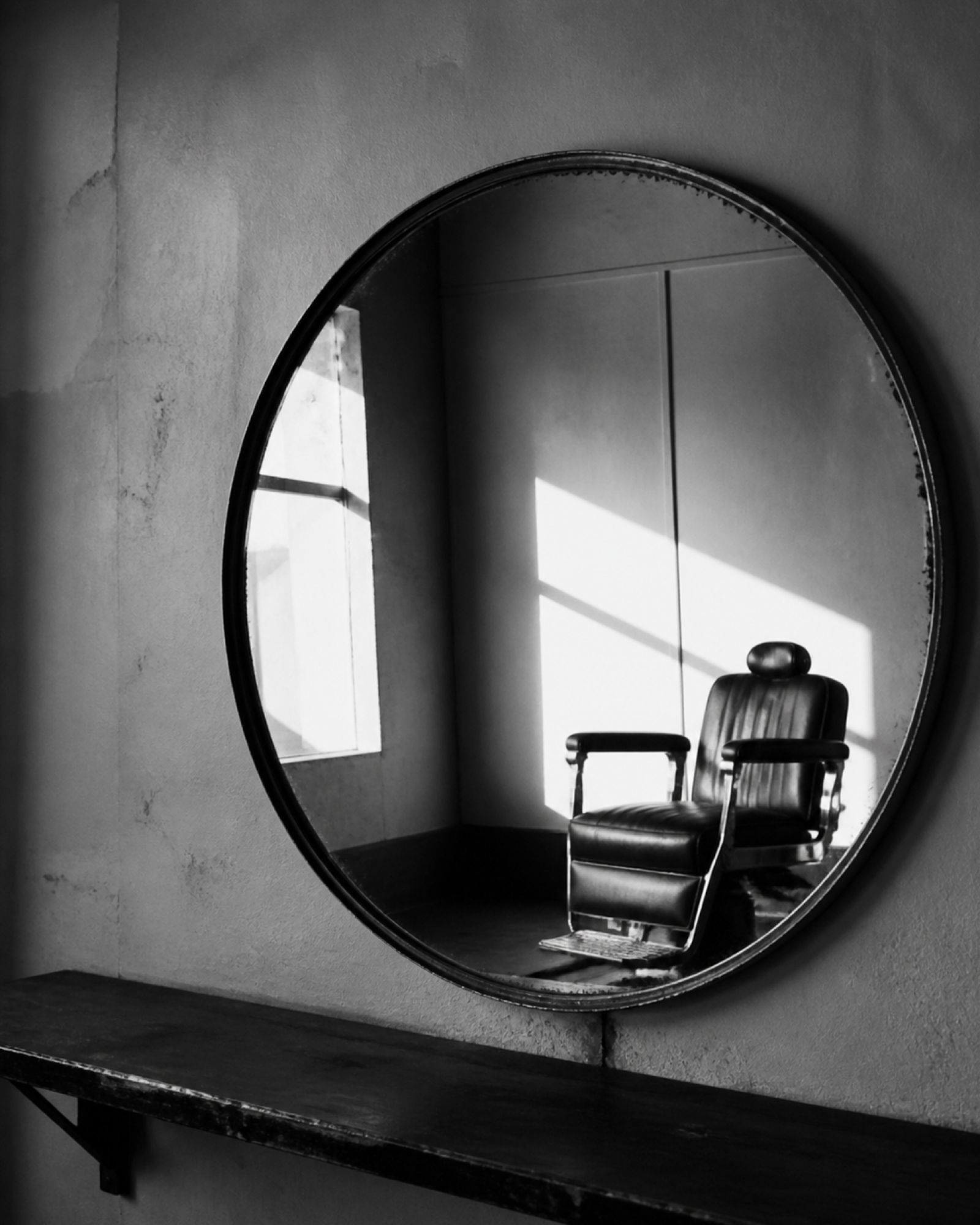 A round barbershop mirror reflecting an empty barber chair