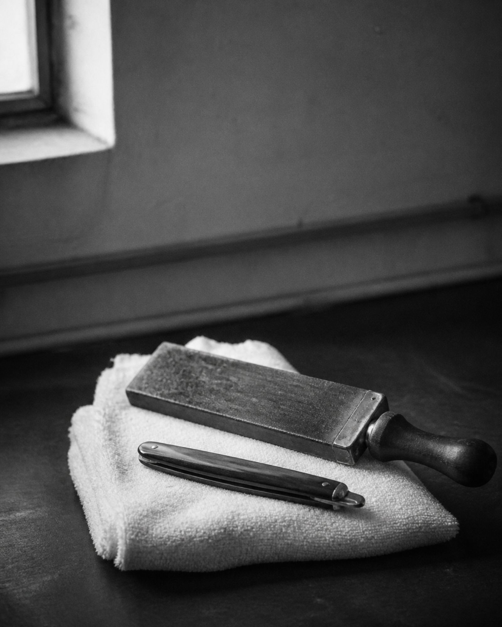A closed straight razor and a leather strop on a folded towel